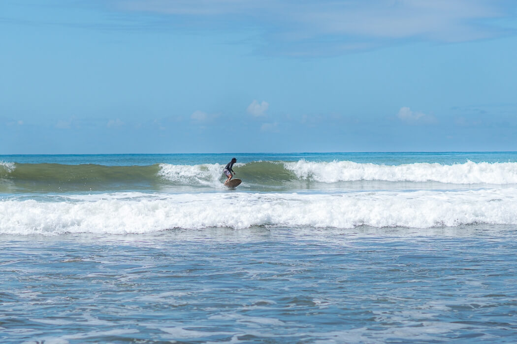 Surfer riding a green wave on a surfboard against bright blue ocean and sky background