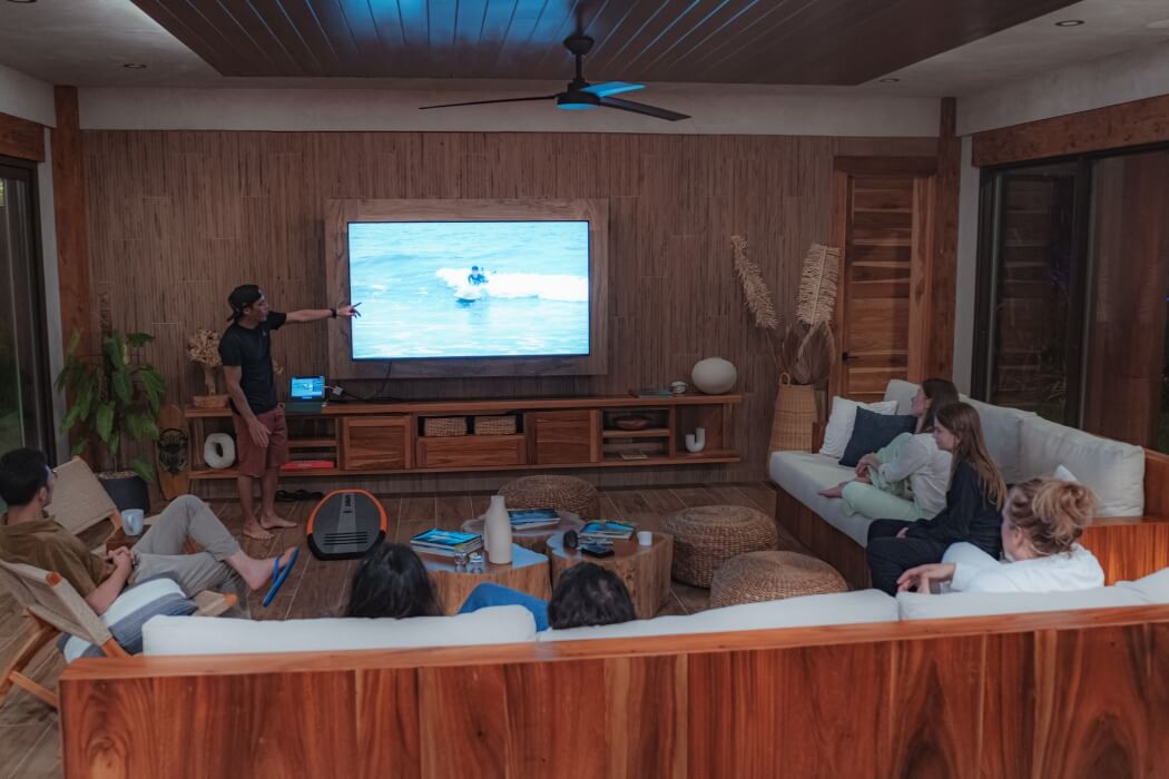 Contemporary wood-paneled living room with large TV showing surfing, comfortable sectional seating, and tropical decor