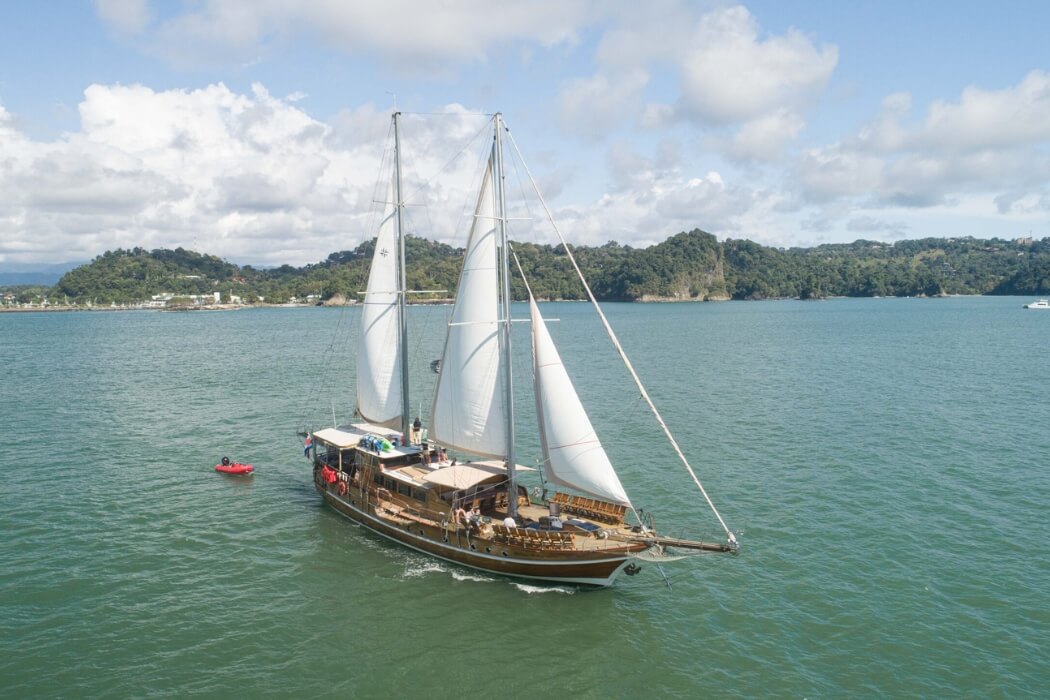 Traditional wooden sailboat with white sails cruising in turquoise waters off Costa Rica's Pacific coast