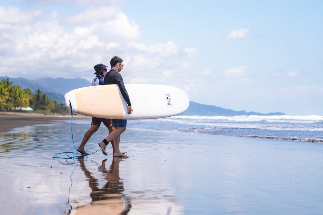 Two surfers walking along tropical beach carrying surfboards in Costa Rica