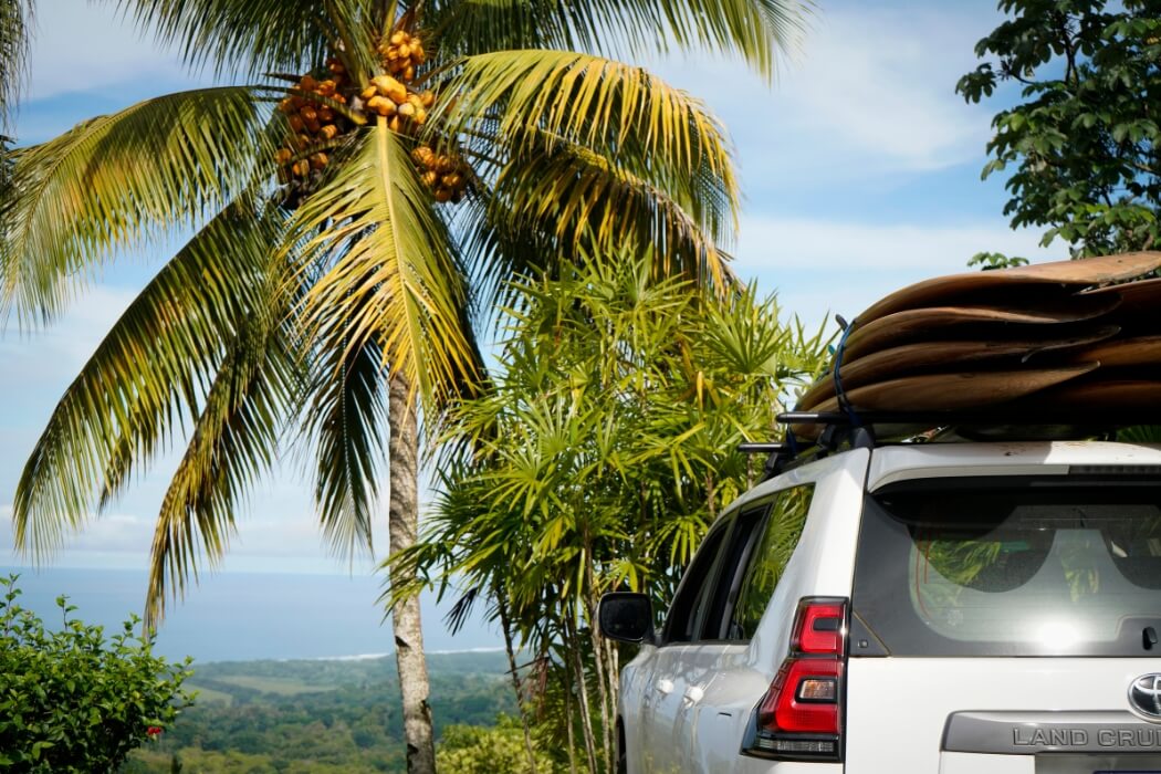 Toyota Land Cruiser loaded with surfboards under palm trees overlooking Costa Rican coast