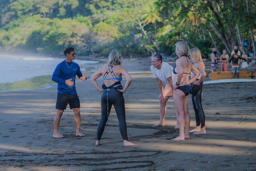 Group of people in athletic wear discussing on tropical beach with lush forest background