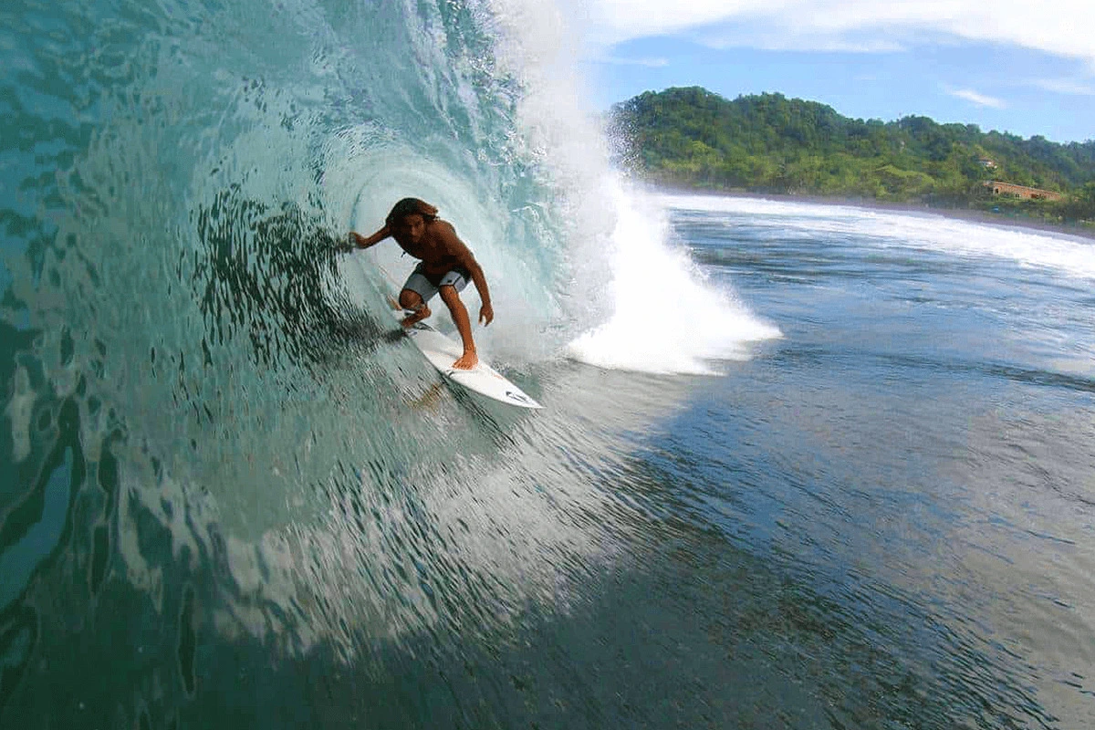 Surfer Riding Left-Hand Point Break at Pavones, Costa Rica Experienced surfer riding a long, peeling left-hand wave at Pavones, Costa Rica, with jungle-lined coastline in the background.