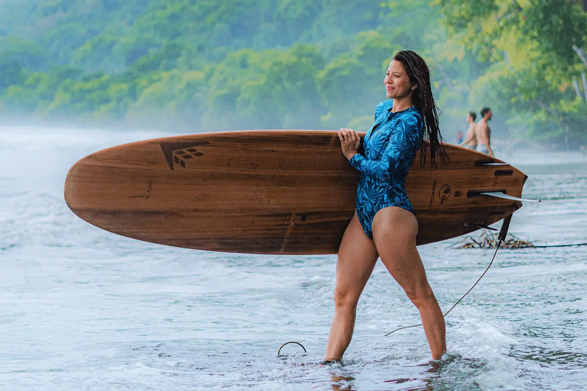 Woman Walking Toward the Ocean with Surfboard in Costa Rica Woman holding a surfboard walking toward the ocean on a tropical beach in Costa Rica, with waves rolling in and palm trees in the background.