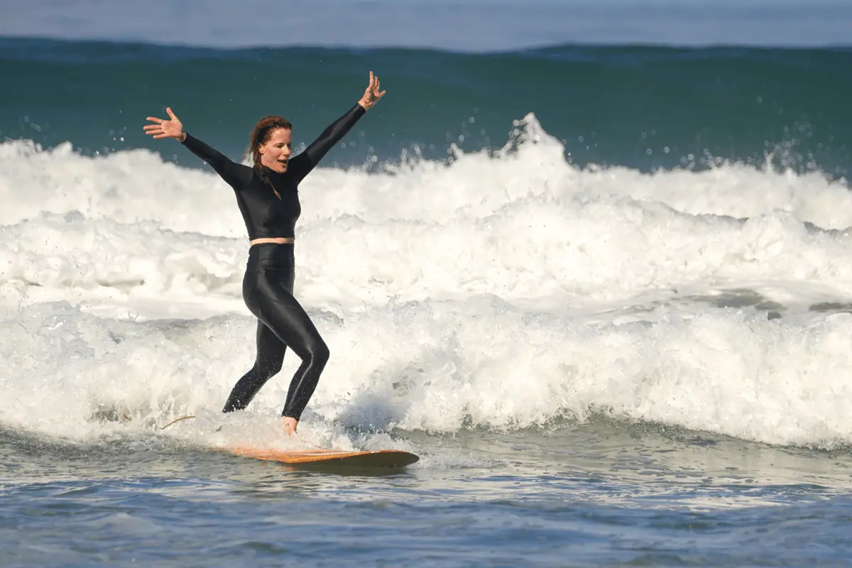 Woman Surfing in Costa Rica in Black Swimwear Woman in black swimwear surfing a clean wave in Costa Rica, with lush rainforest in the background.
