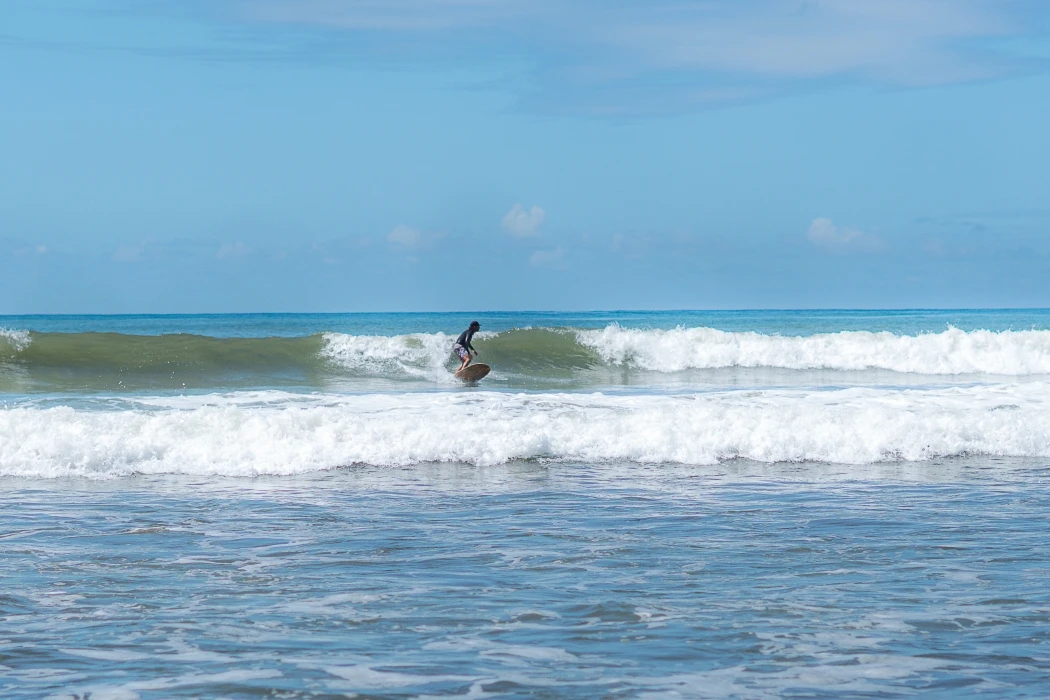 Surfer Riding Ocean Wave Surfer riding a green ocean wave on sunny day with white foam and blue sky at tropical surf beach