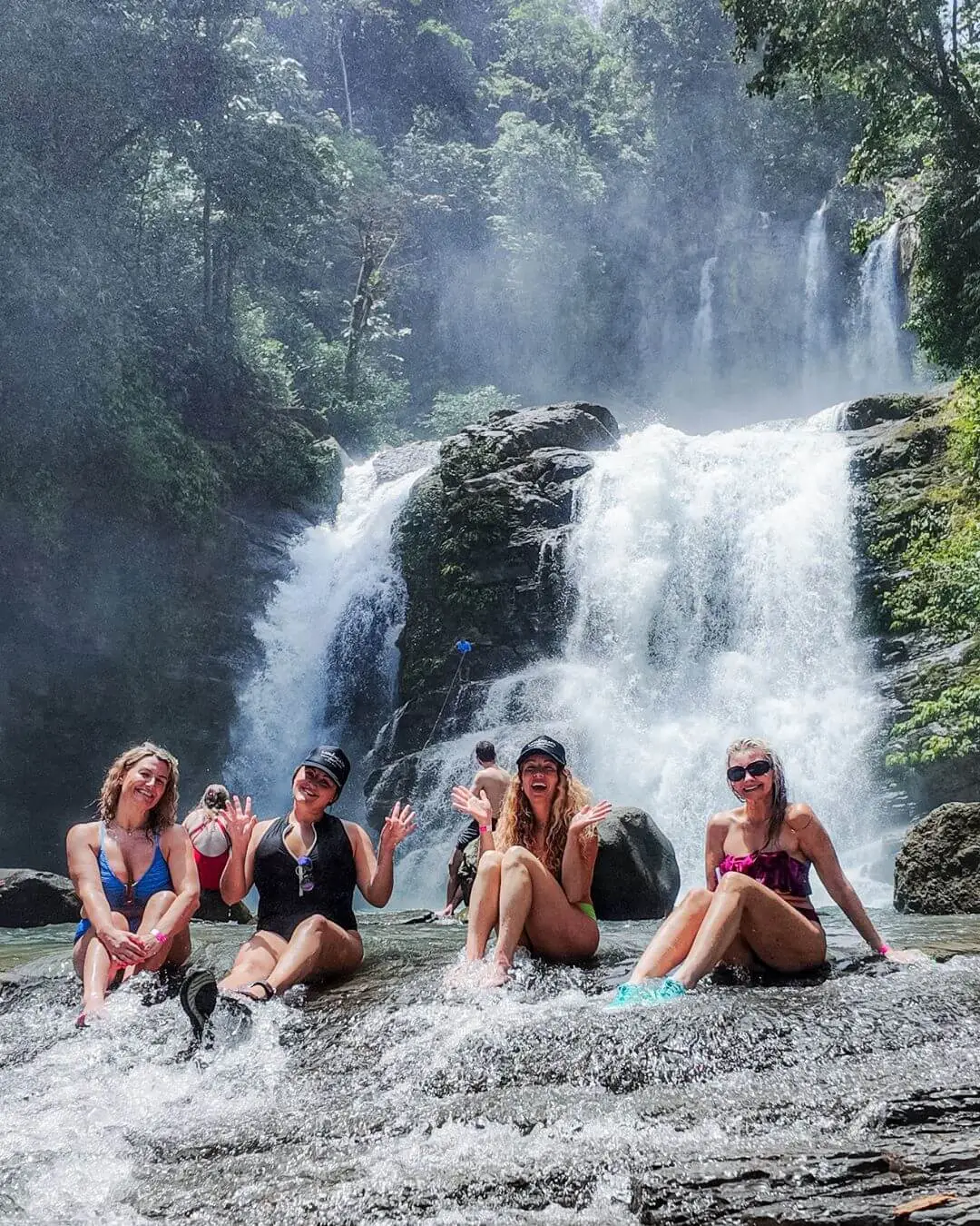 Four women sitting at the base of a waterfall in Costa Rica