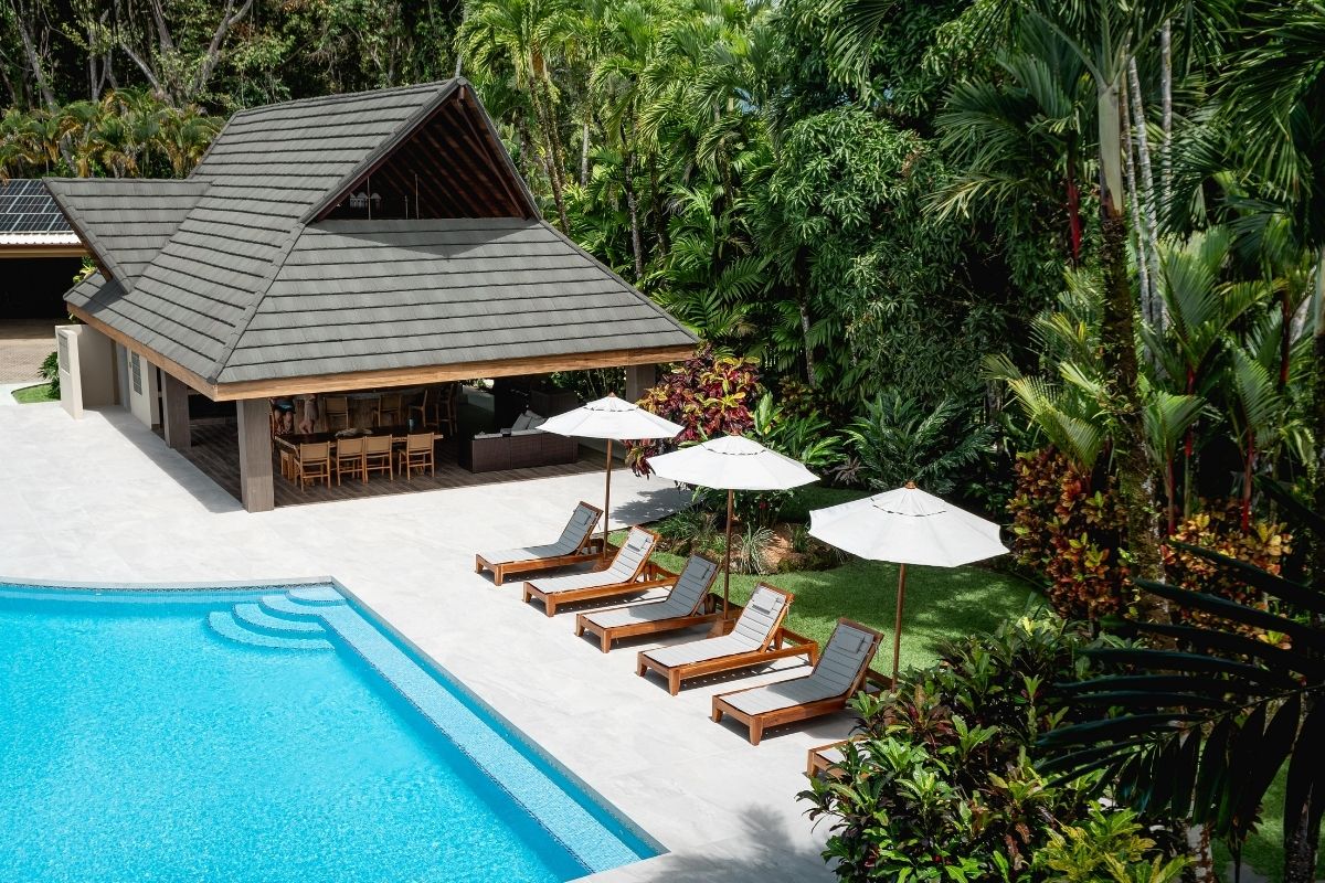Tropical luxury lodge with a swimming pool, lounge chairs, umbrellas, and an open-air bar surrounded by lush jungle greenery.