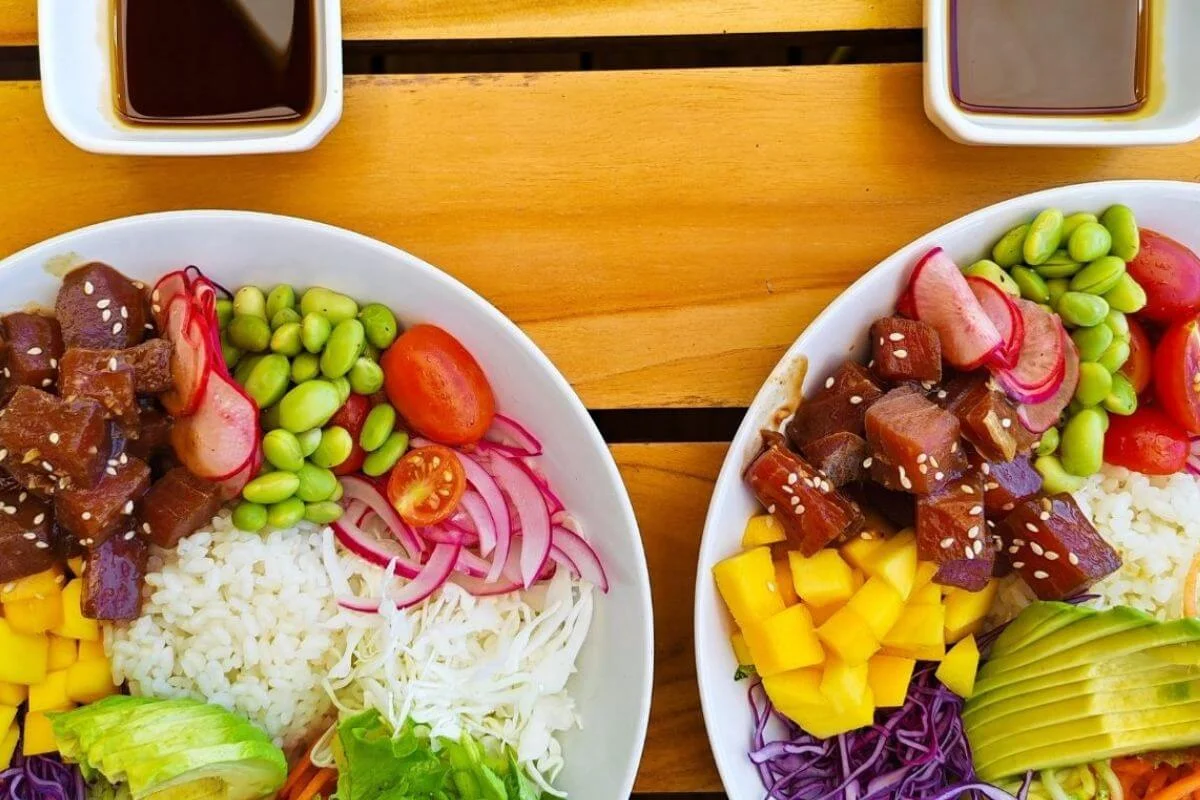 Two colorful poke bowls with tuna, mango, avocado, edamame, and rice on a wooden table