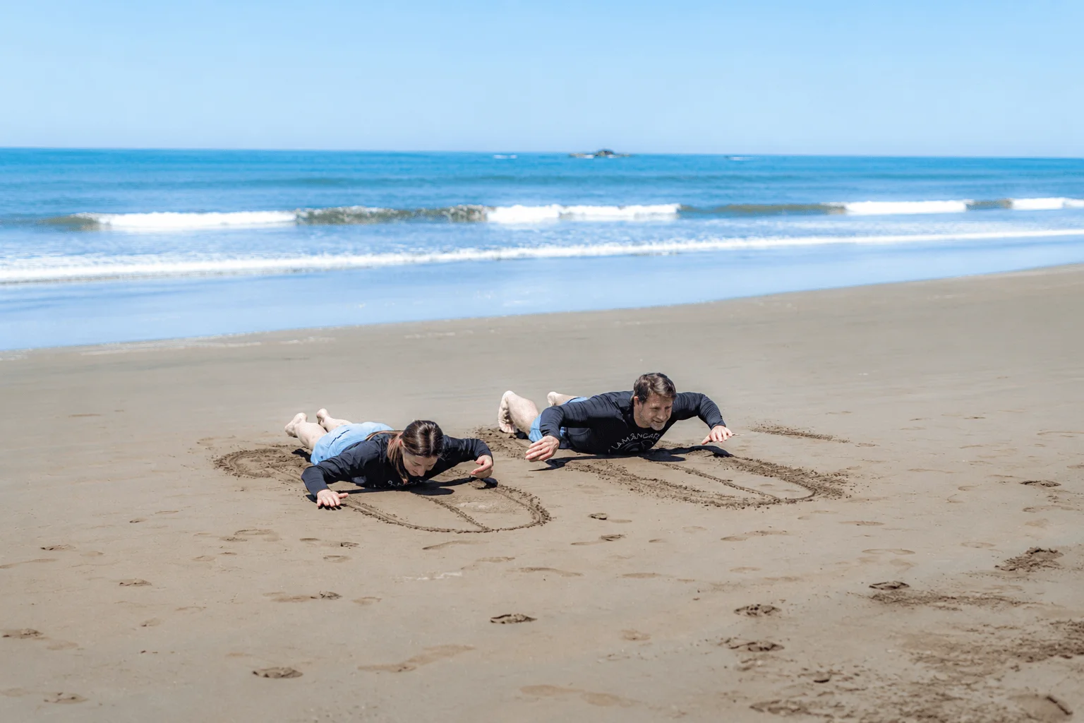 Couple practicing surf pop up technique on sandy beach