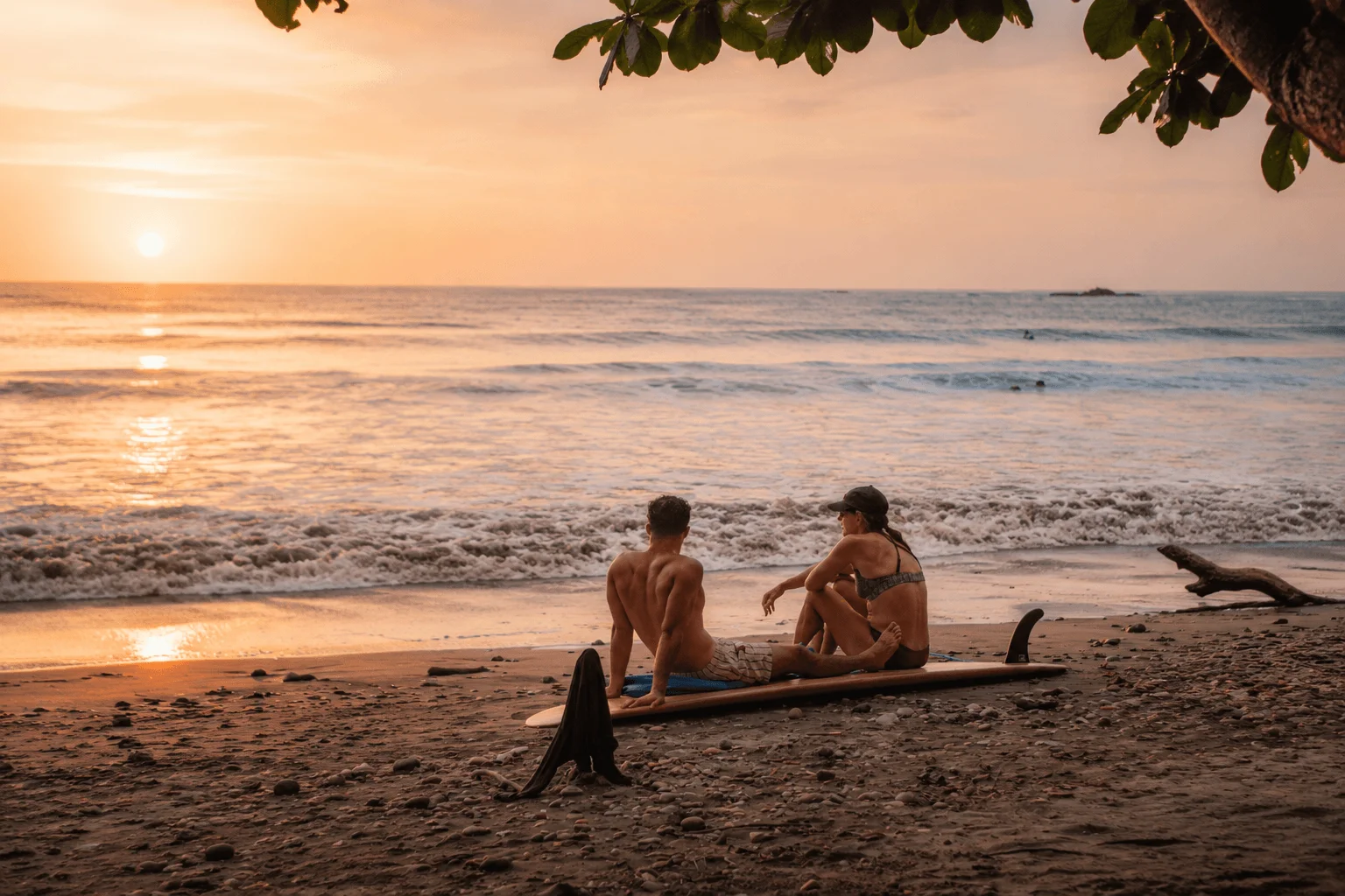 Couple relaxing on surfboard watching sunset over ocean