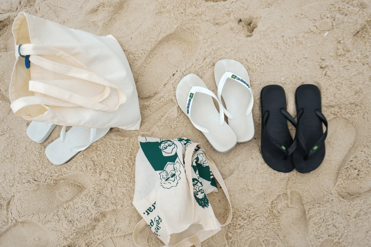 Two pairs of flip flops and canvas tote bags laid out on white beach sand
