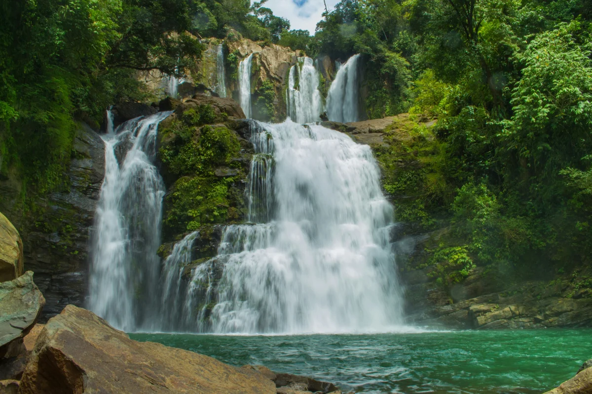 Nauyaca Waterfalls flowing over mossy rocks into a turquoise pool surrounded by rainforest