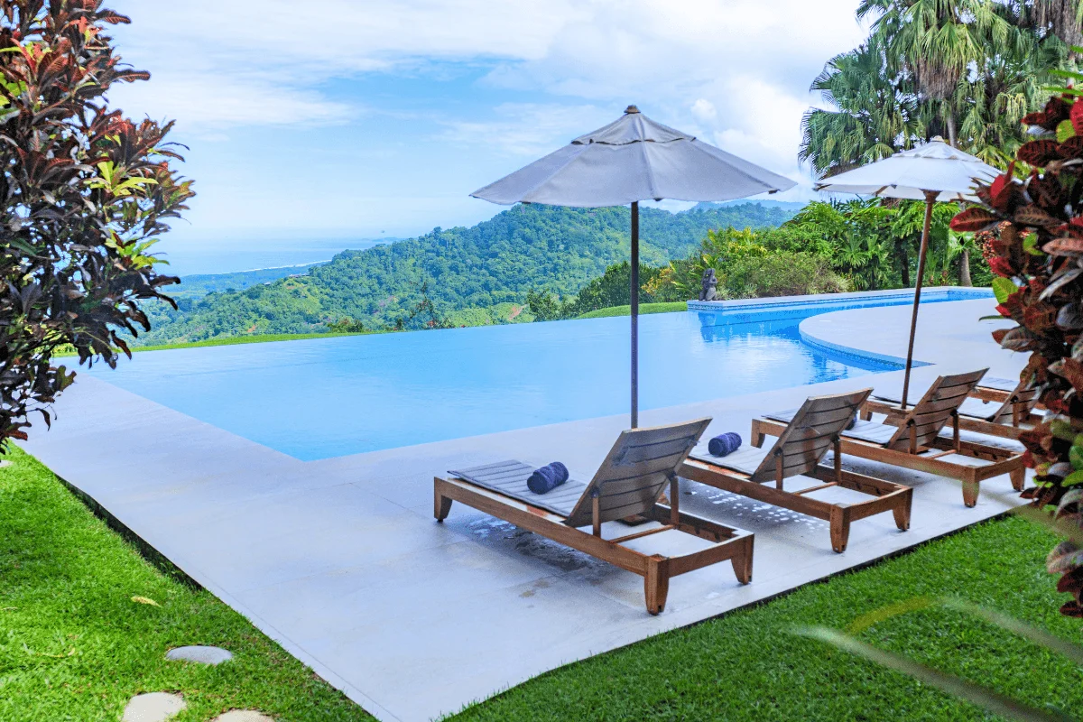 Wooden lounge chairs and umbrellas beside an infinity pool overlooking rainforest and ocean in Costa Rica