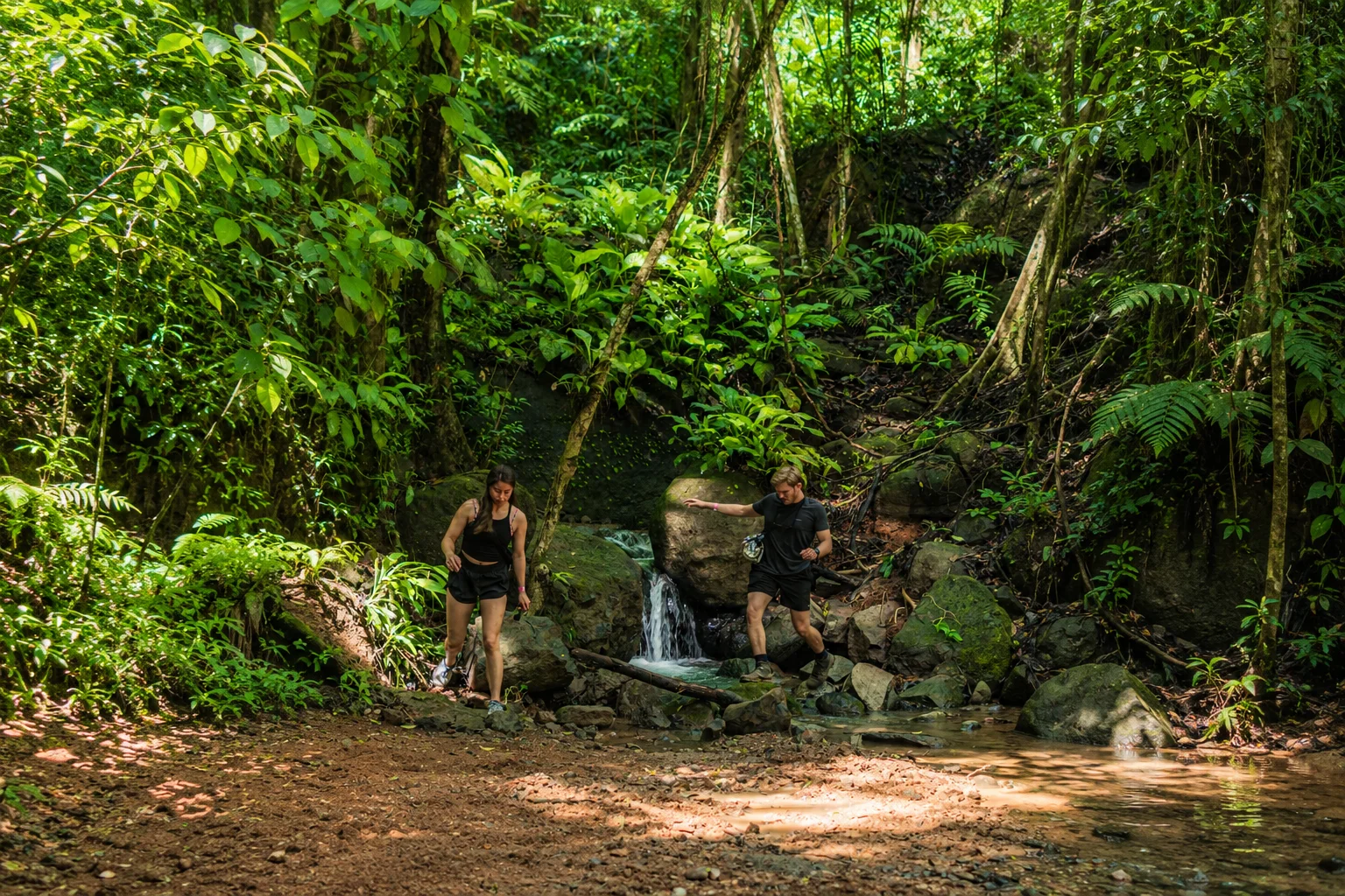 Couple crossing a small stream on a rainforest trail on the hike to Nauyaca Waterfalls