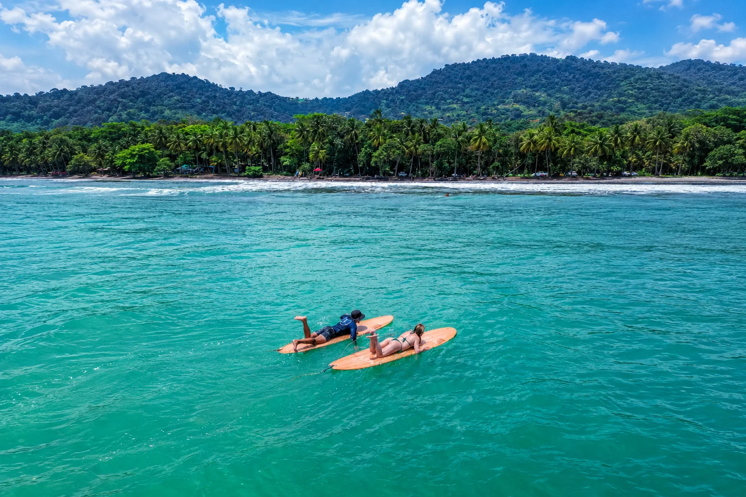 Two guests lying on wooden surfboards in calm turquoise water near Lamangata