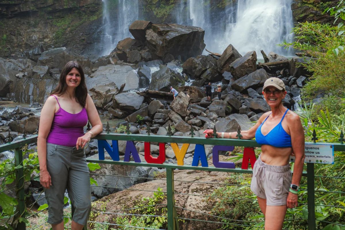 Two guests posing next to the colorful Nauyaca sign with the waterfalls in the background