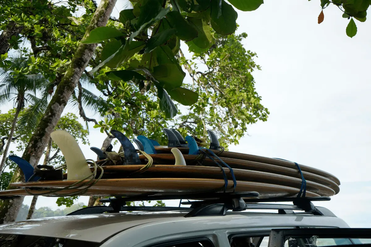 Stack of surfboards strapped securely to the roof rack of an SUV vehicle parked beneath tropical trees.