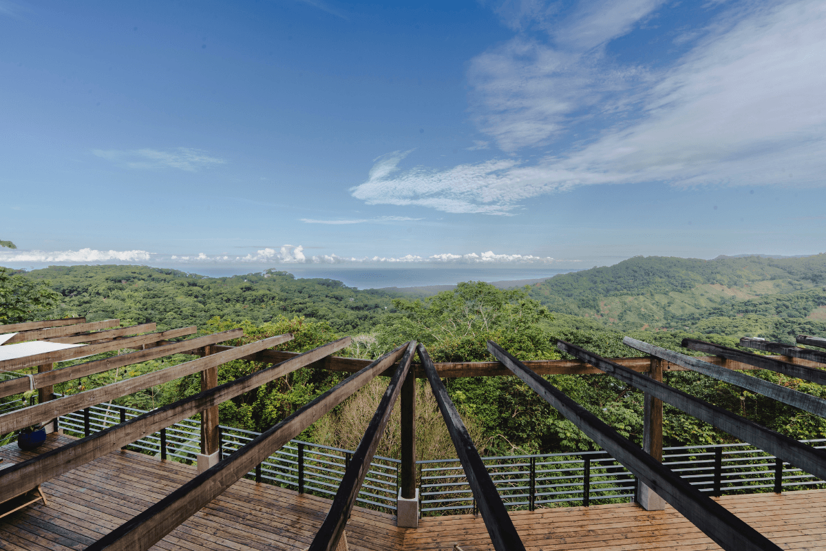 Wooden pergola deck overlooking rainforest-covered hills and the Pacific Ocean on the horizon at La Mangata near Dominical